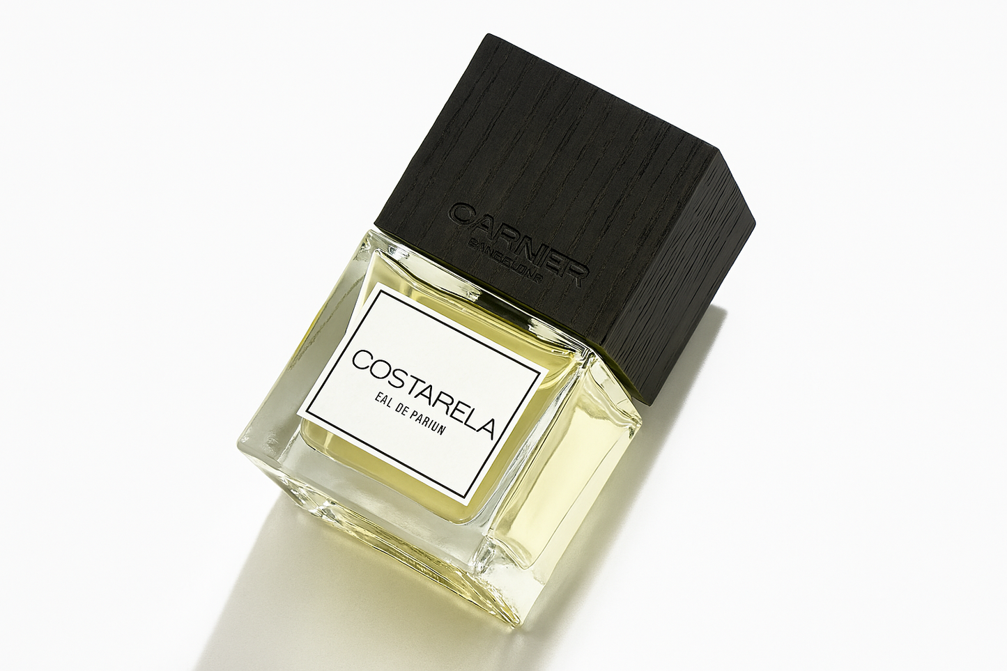 Eine schräge Nahaufnahme eines Parfümflakons von „Costarela Eau de Parfum“ von Carner Barcelona. Der rechteckige Glasflakon mit blassgelber Flüssigkeit hat eine strukturierte schwarze Holzverschraubung mit eingeprägtem Markennamen. Die weiße Etikette mit schwarzer Schrift ist gut lesbar. Der Hintergrund ist neutral weiß, mit einem weichen natürlichen Schatten rechts unten.