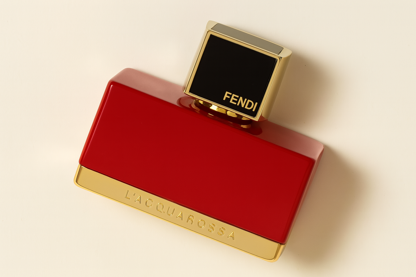 Ein rechteckiger, glänzend roter Parfumflakon liegt leicht geneigt auf einer hellen, neutralen Fläche. Der Flakon ist mit goldfarbenen Akzenten versehen: unten ist „L'ACQUAROSSA“ eingeprägt, oben befindet sich ein quadratischer schwarzer Deckel mit goldener Umrandung und der Aufschrift „FENDI“. Der Gesamteindruck ist luxuriös, modern und kraftvoll. Ein sanfter Schatten verleiht dem Bild Tiefe.