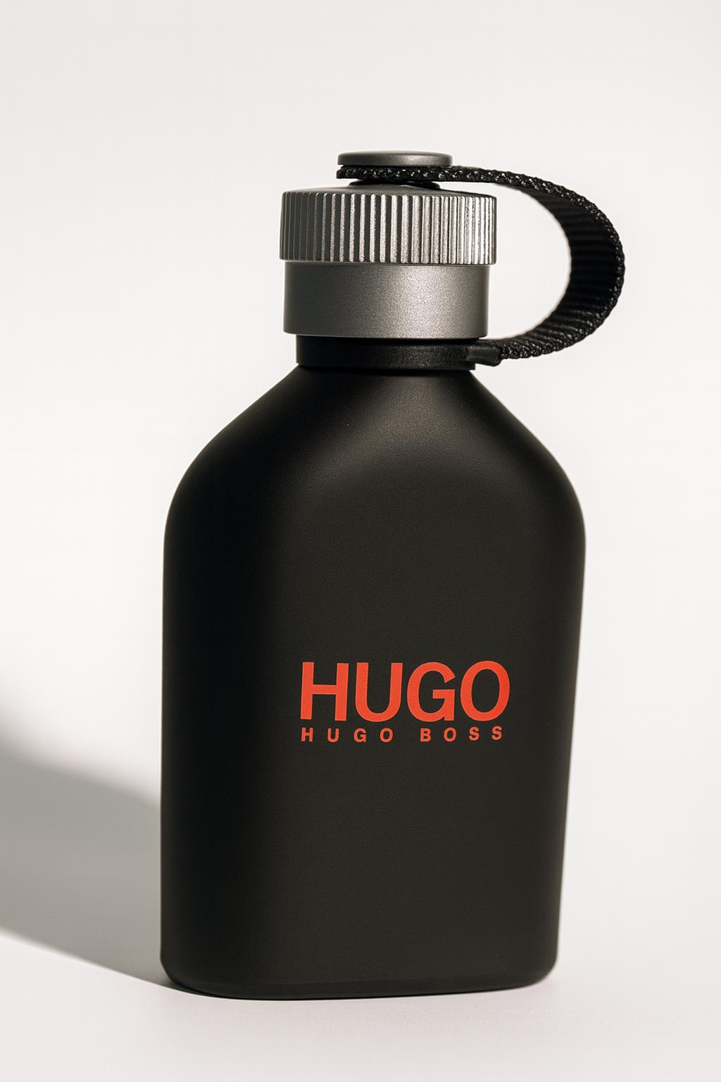 Schräg dargestelltes schwarzes Hugo Boss „Hugo Just Different“ Eau de Toilette mit silbernem Schraubverschluss und schwarzem Stoffband, vor neutralem Hintergrund, mit weichem Schatten.
