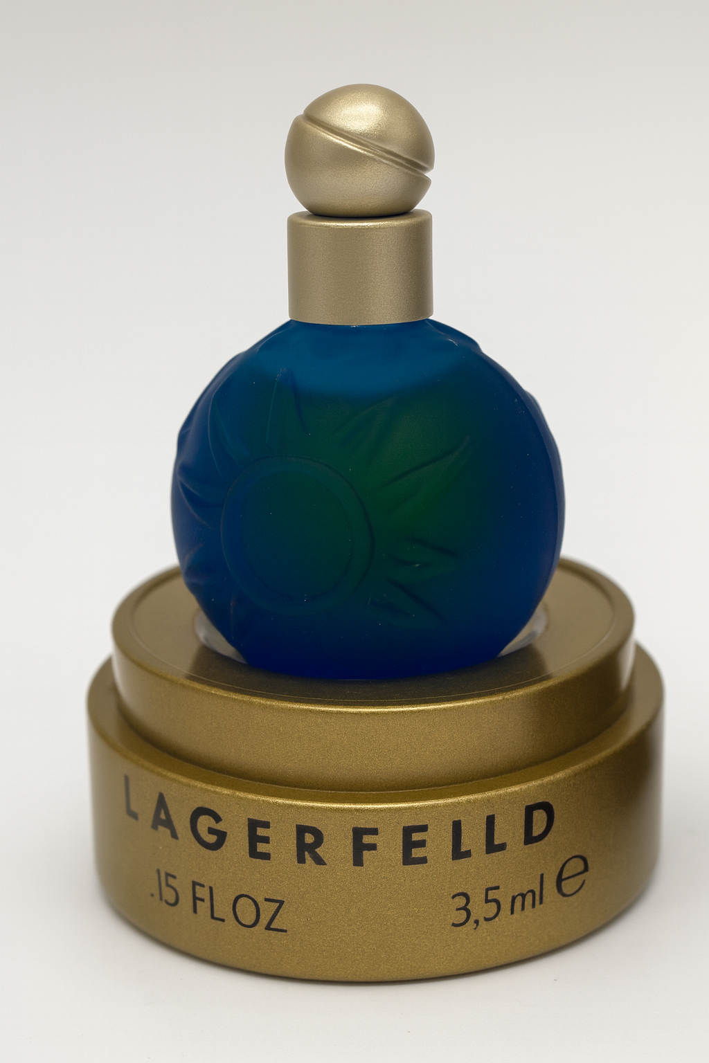 Ein kleines, kugelförmiges, tiefblaues Parfumfläschchen von Karl Lagerfeld „Sun Moon Stars“ mit geprägten Sonnenmotiven, goldener Kappe und goldenem Sockel, leicht nach hinten gekippt, auf neutralem Hintergrund.