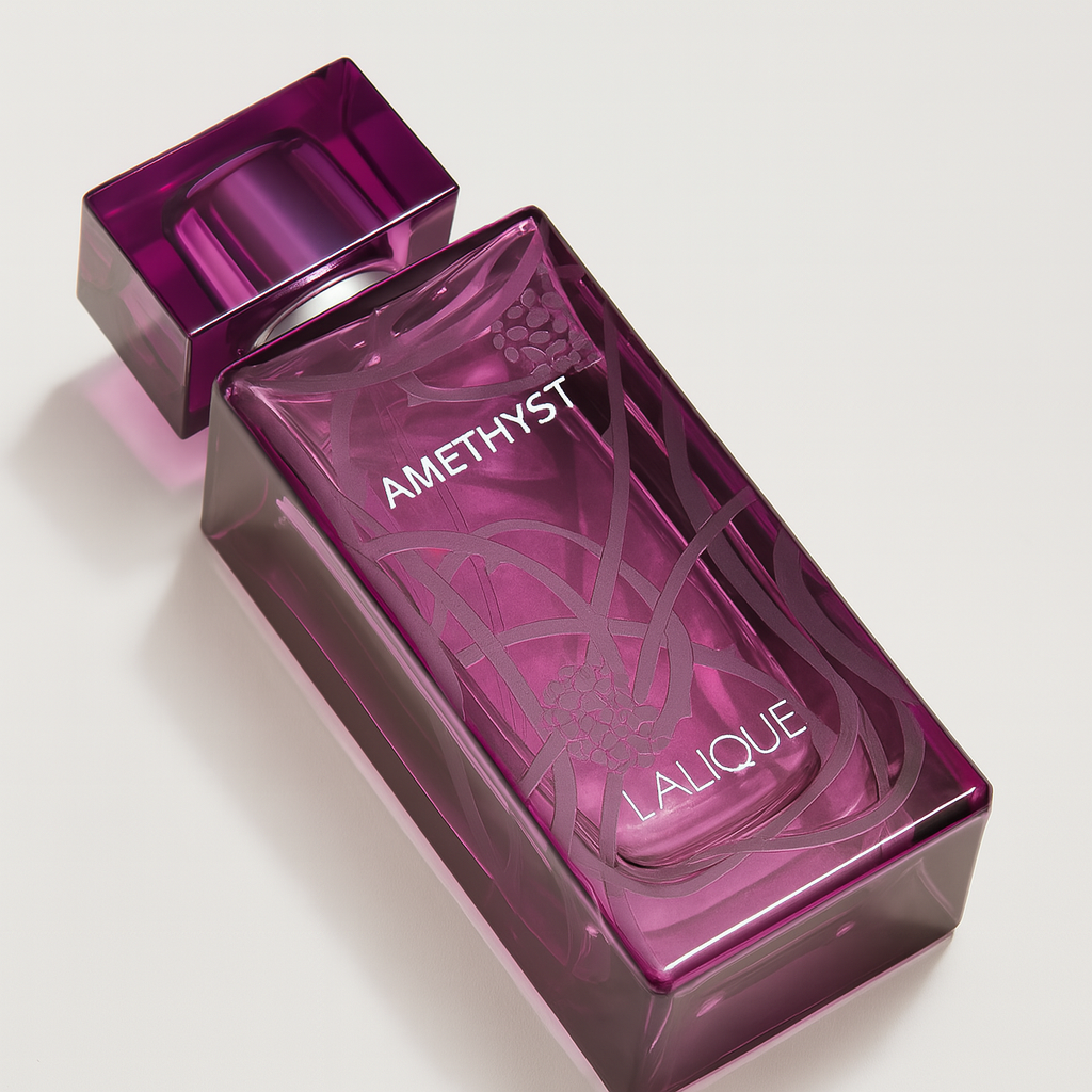 Ein violettes Parfumflakon von Lalique „Amethyst“ liegt leicht geneigt auf einer neutralweißen Fläche. Der eckige Flakon aus transparentem Glas zeigt zarte Gravuren mit Beeren- und Rankenmotiven. Die Aufschrift „AMETHYST LALIQUE“ ist deutlich sichtbar. Ein weicher Schatten rundet das hochwertige Bild ab.