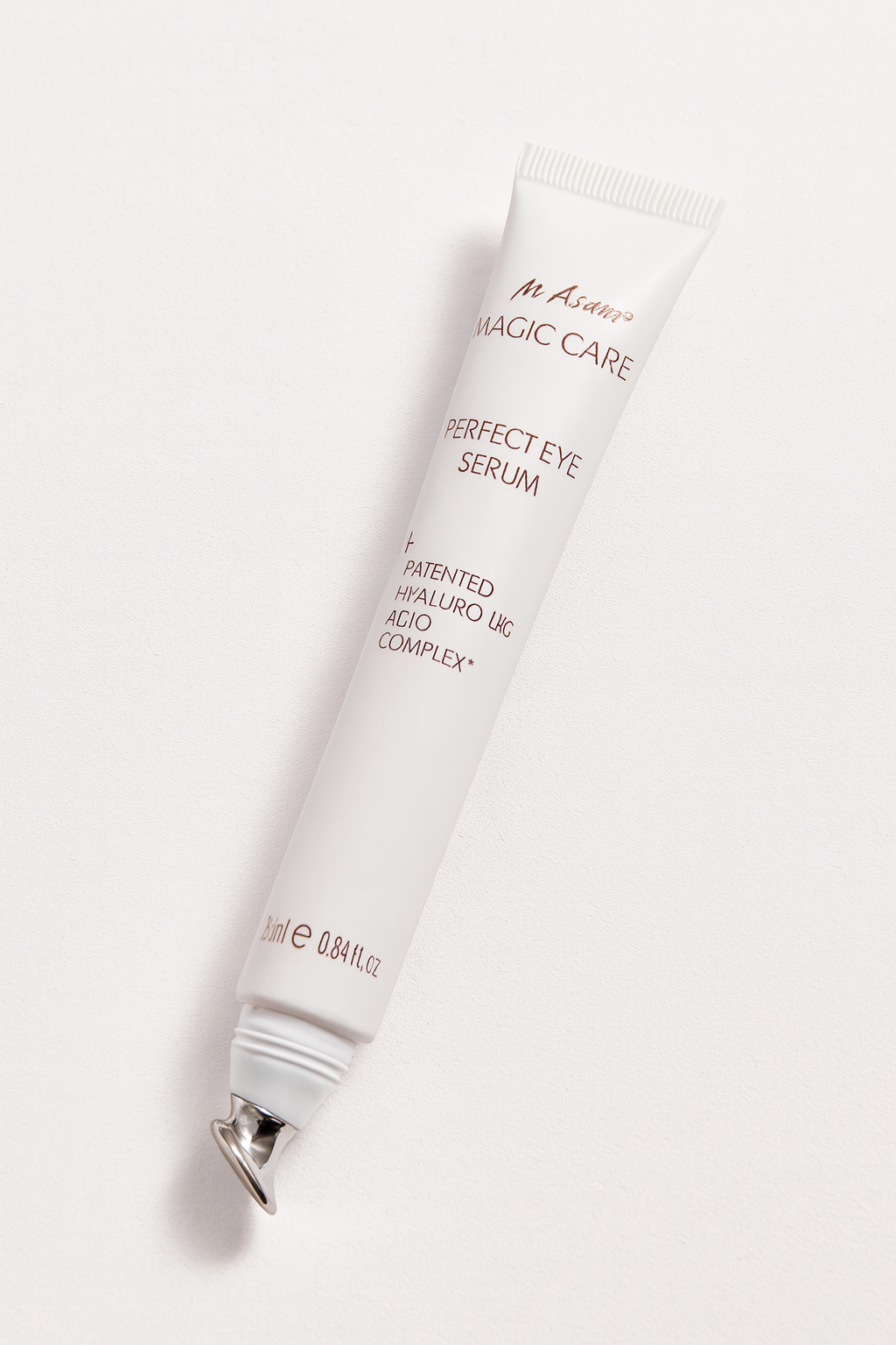 Eine weiße Tube des M. Asam Magic Care Perfect Eye Serum liegt diagonal auf einem neutralen Hintergrund. Der Applikator ist silberfarben und leicht gebogen, während die elegante roségoldene Aufschrift klar erkennbar ist. Ein weicher Schatten unterstreicht die Tiefe und Rundung der Tube.