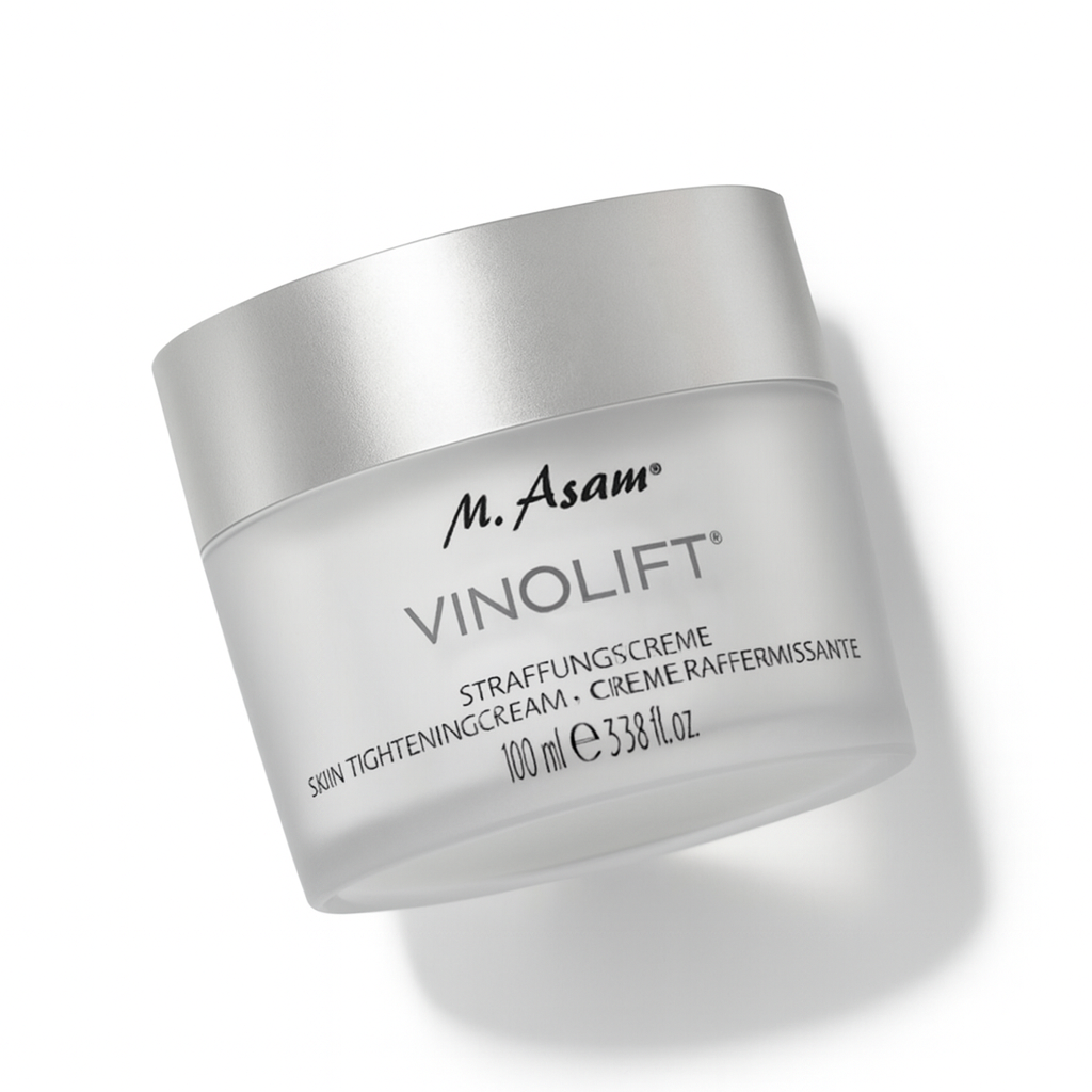 Ein matt-transparenter Tiegel der M. Asam VINOLIFT Straffungscreme mit silbernem Deckel liegt leicht nach hinten gekippt auf weißem Hintergrund. Die schwarze Aufschrift ist klar lesbar, und der Tiegel wirft einen weichen Schatten.
