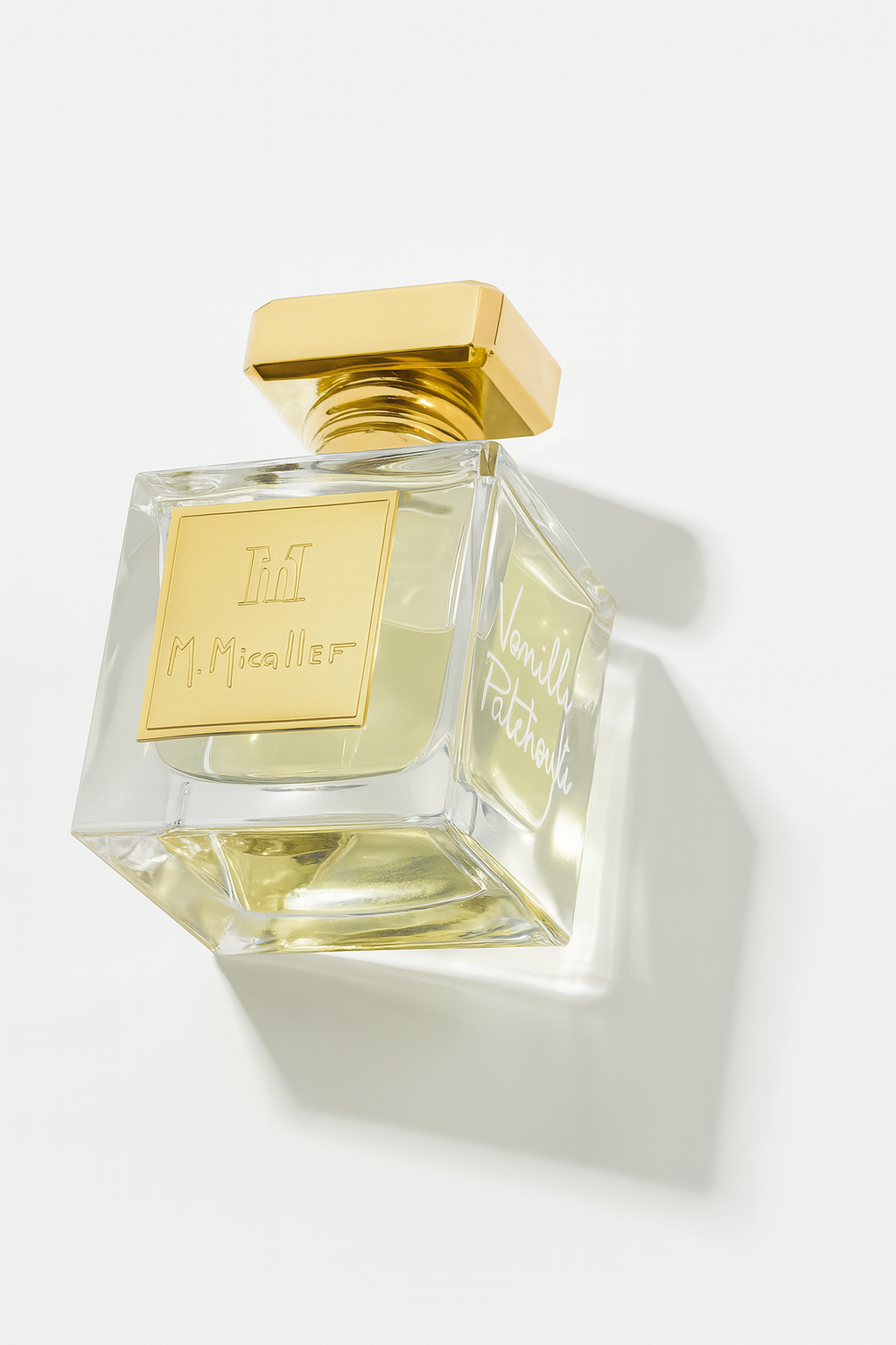 Ein kantiges Glasflakon des M. Micallef Vanille Patchouli Parfums, leicht nach hinten geneigt, mit goldenem Verschluss und goldenem Frontschild, das Logo und den Namen trägt. Das Flakon steht vor neutralem Hintergrund und wirft einen weichen Schatten.