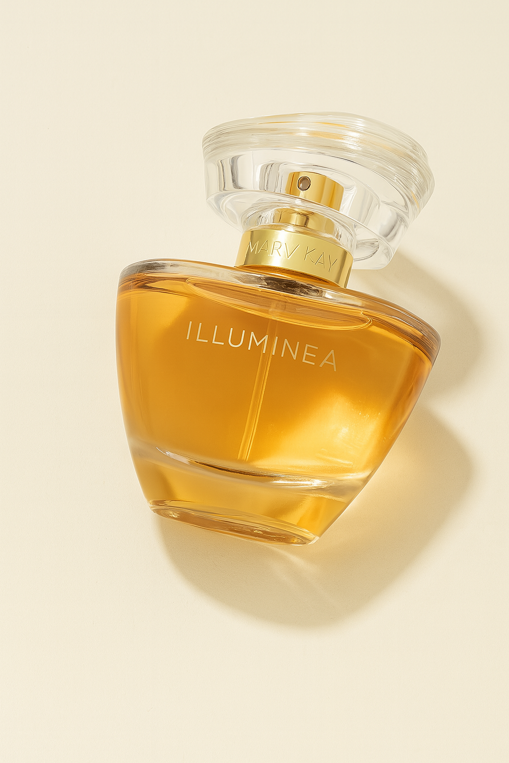 Ein schräg nach hinten gekipptes Parfumflakon „Illuminea“ von Mary Kay, mit goldenem Sprühkopf und transparenter Verschlusskappe. Der Flakon enthält eine bernsteinfarbene Flüssigkeit und wirft einen weichen Schatten auf einen neutralen cremefarbenen Hintergrund.