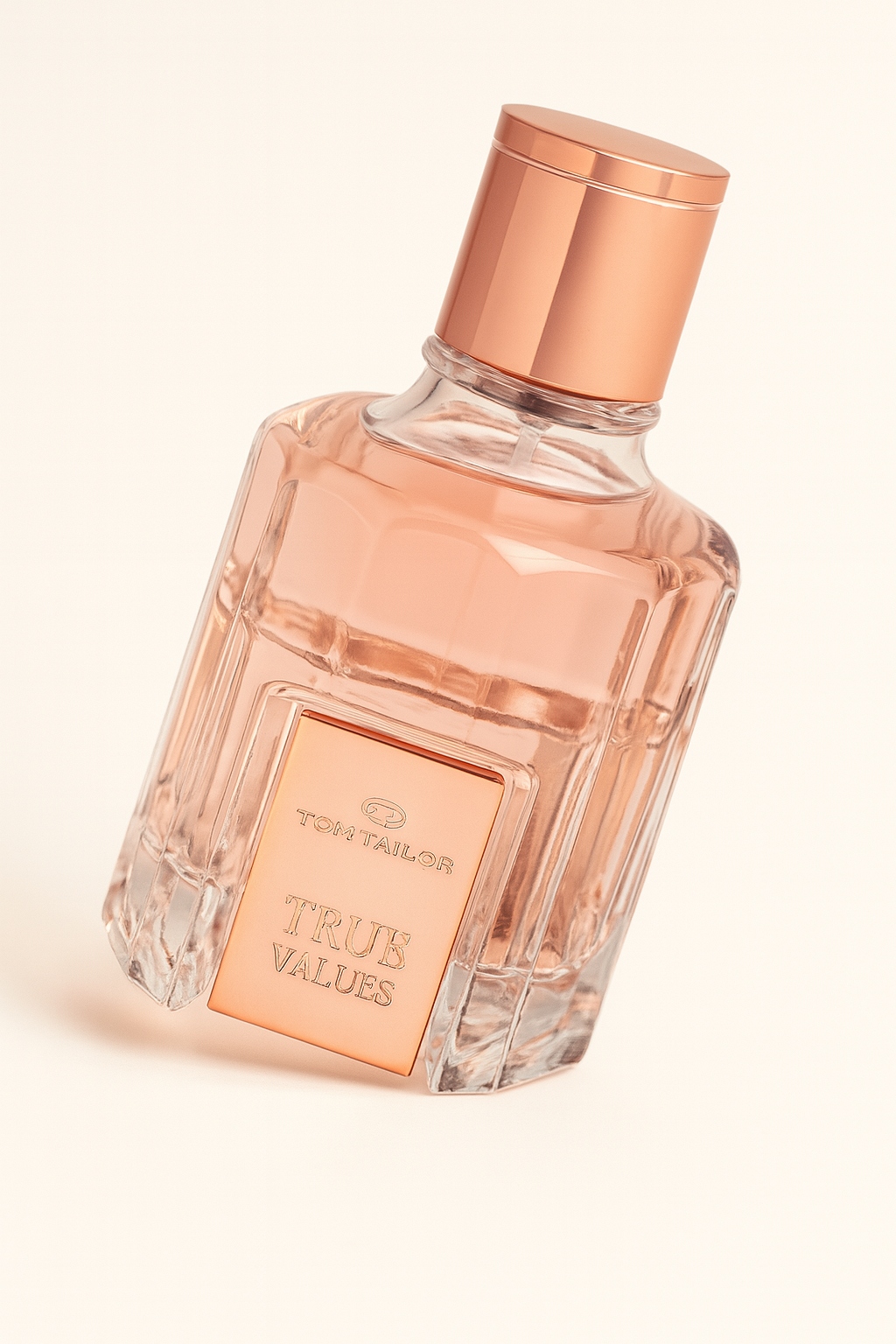 Ein rosa-transparentes Parfumflakon von „Tom Tailor TRUE VALUES“ steht leicht zur Seite geneigt auf hellem, neutralem Hintergrund. Die Vorderseite zeigt eine roségoldene Plakette mit Marken- und Produktname. Der zylindrische Deckel ist ebenfalls roségoldfarben. Ein sanfter Schatten verläuft nach rechts unten.