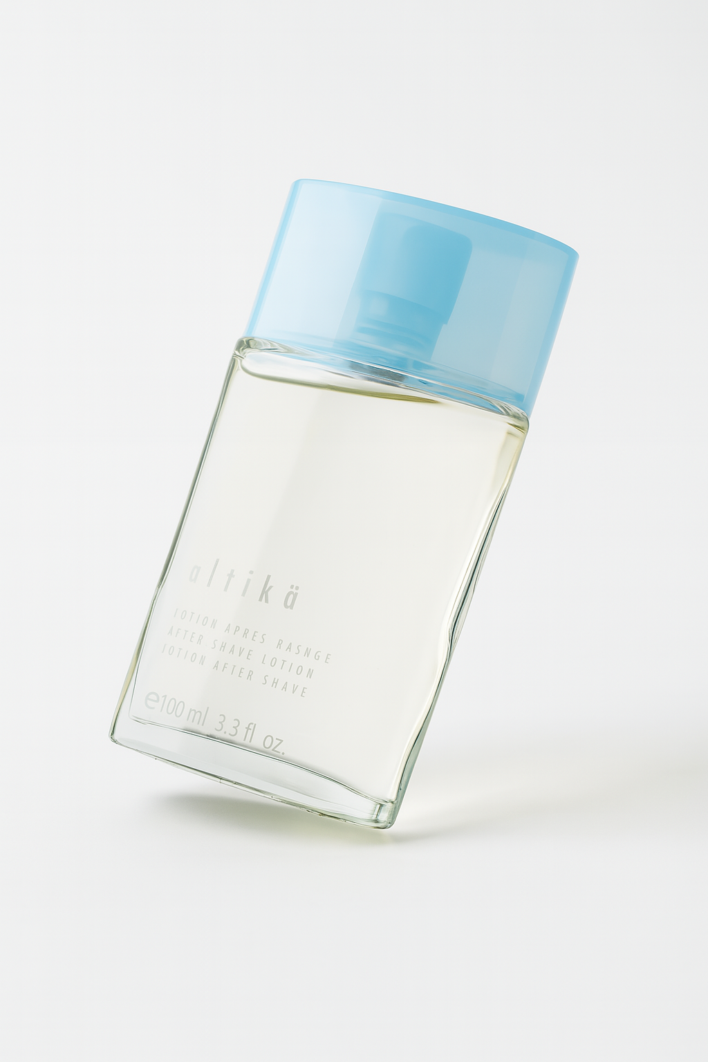 Ein rechteckiges, klares Glasflakon mit hellblauem Deckel, das leicht nach hinten geneigt auf einem weißen, neutralen Hintergrund steht. Die Aufschrift "altikä – After Shave Lotion" ist auf der Vorderseite sichtbar. Ein weicher Schatten fällt nach hinten rechts.