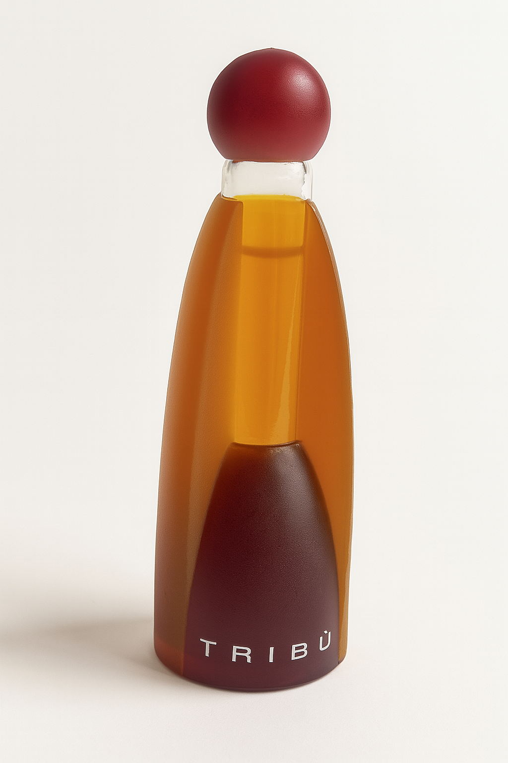 Das Bild zeigt das Tribu Parfumflakon von Benetton. Es ist ein hohes, schlankes Glasflakon in einem warmen Bernsteinton mit einem roten, kugelförmigen Verschluss. Der Markenname „TRIBÙ“ ist am unteren Rand des Flakons in weißen Buchstaben sichtbar. Das Flakon steht aufrecht vor einem neutralen Hintergrund und wirft einen weichen Schatten.