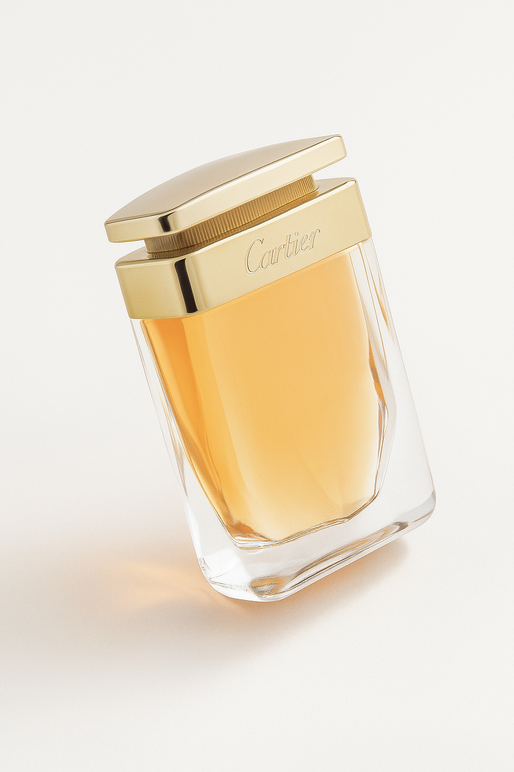 Ein transparentes Cartier-Parfumflakon mit goldenem Verschluss und bernsteinfarbener Flüssigkeit ist leicht zur Seite gekippt vor einem neutralen, hellen Hintergrund abgebildet. Die goldene Aufschrift „Cartier“ ist klar lesbar, ein weicher Schatten verläuft sanft rechts unterhalb der Flasche.