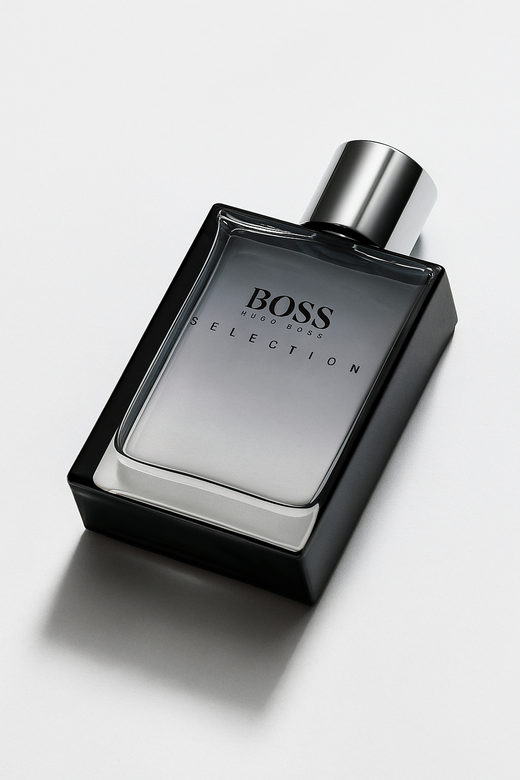 Ein rechteckiges Parfumflakon von Hugo Boss „Selection“ liegt leicht nach hinten gekippt auf einer hellgrauen Oberfläche. Die Vorderseite mit dem Logo ist gut sichtbar. Das Glas wirft einen natürlichen, weichen Schatten.