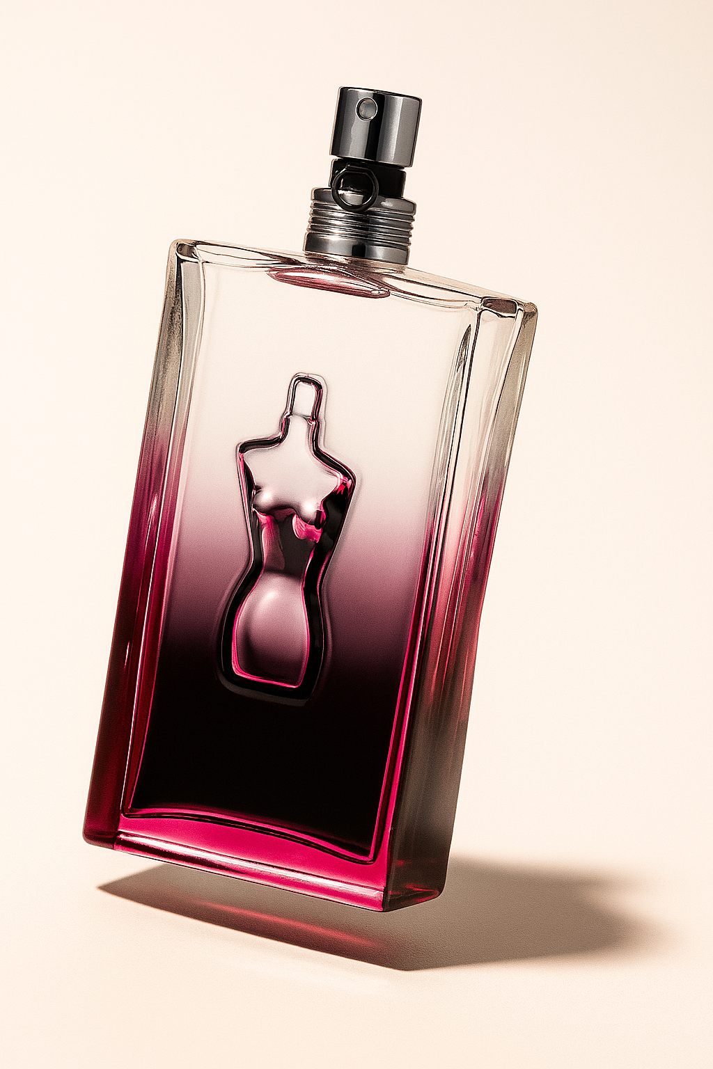 Ein schräg stehender, rechteckiger Parfümflakon von Jean Paul Gaultier, mit einem stilisierten Frauenkörper in Reliefoptik in der Mitte. Der Flakon verläuft farblich von klarem Glas zu einem dunklen Magenta und wirft einen weichen, natürlichen Schatten auf einem neutralen Hintergrund.