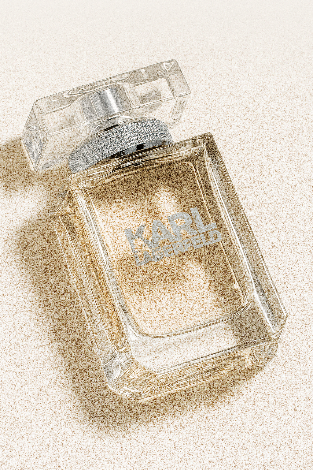Eine fotografische Darstellung eines leicht nach hinten geneigten, eckigen Parfumflakons von Karl Lagerfeld. Der Flakon besteht aus klarem Glas, hat einen silbernen, strukturierten Hals und einen transparenten, rechteckigen Verschluss. Auf dem Flakon ist in silberner Schrift der Markenname "KARL LAGERFELD" zu sehen. Der Hintergrund ist neutral und der Flakon wirft einen weichen, natürlichen Schatten.
