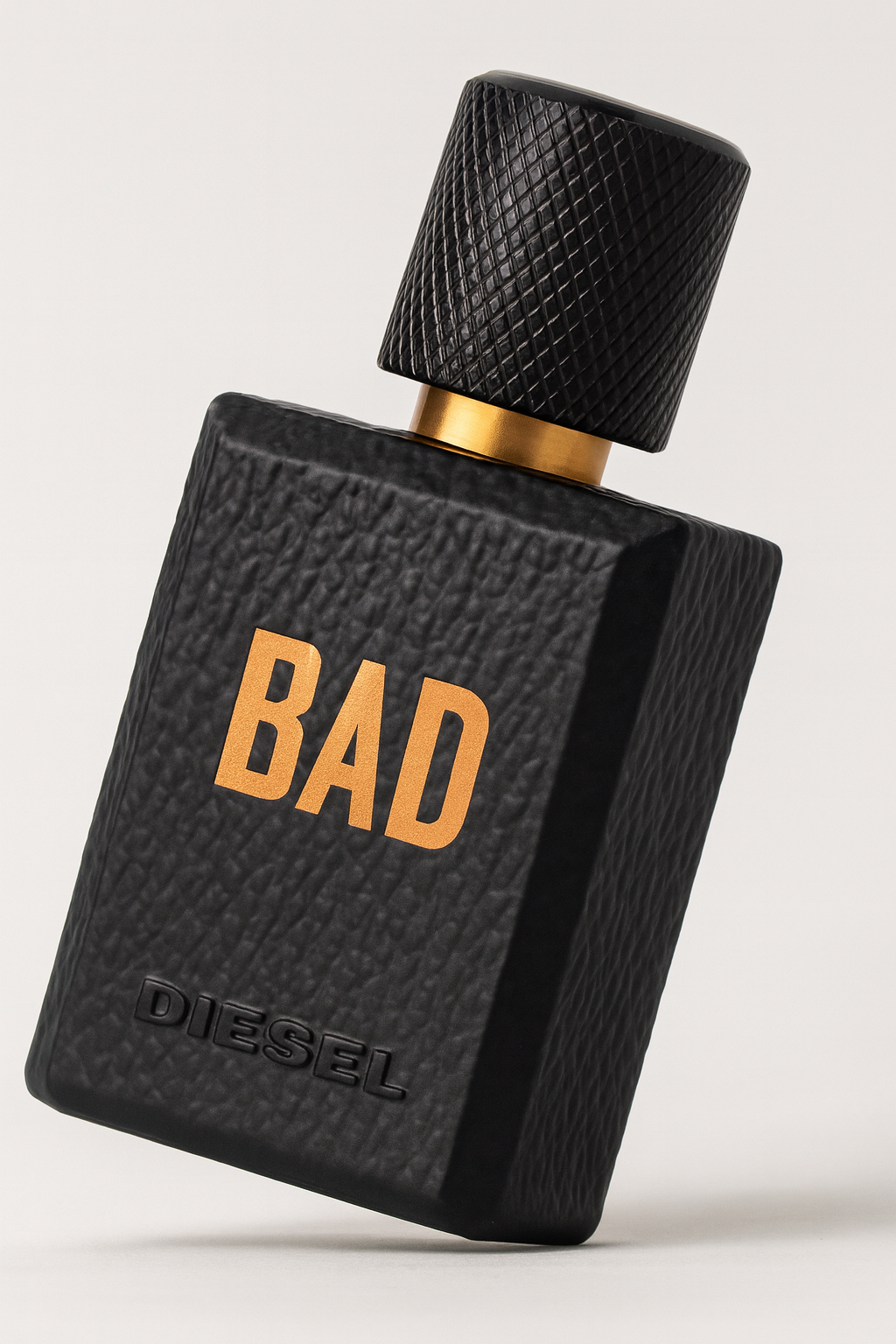 Schwarzer, rechteckiger Flakon des Diesel „BAD“ Eau de Toilette, leicht nach hinten gekippt, mit geprägter Lederoptik-Oberfläche, goldenem Schriftzug „BAD“ und schwarzem Schraubverschluss mit goldener Zierkante, vor neutralem Hintergrund.