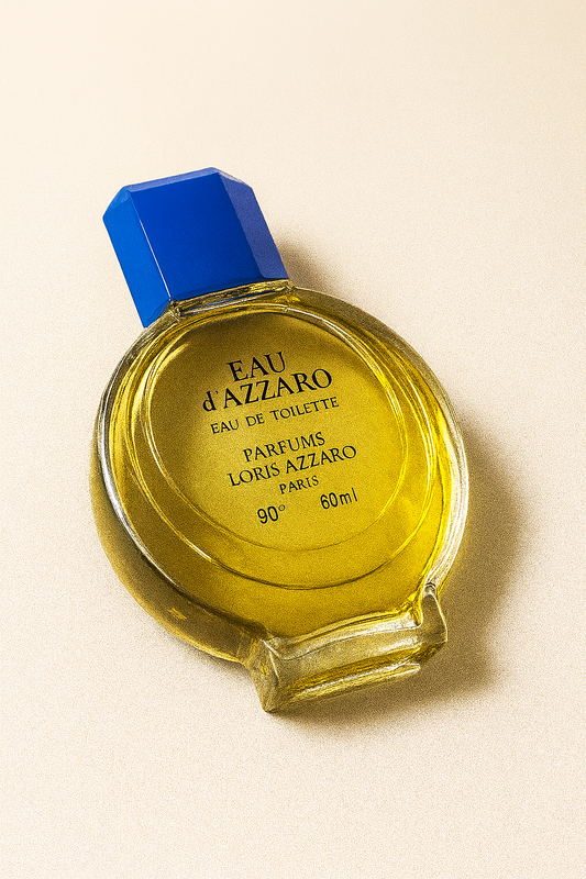 Ein geneigtes Eau d’Azzaro Eau de Toilette Flakon mit blauer Verschlusskappe liegt auf einem neutralen Untergrund. Die goldgelbe Flüssigkeit reflektiert sanftes Licht, der Flakon wirft einen weichen Schatten, während die Beschriftung klar lesbar bleibt.