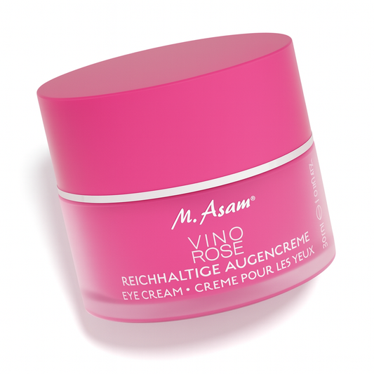 Ein pinkfarbener Tiegel der M. Asam VINO ROSE Reichhaltigen Augencreme liegt leicht schräg nach hinten gekippt auf weißem Hintergrund. Der Deckel ist ebenfalls pink mit silbernem Rand, die weiße Beschriftung auf der Vorderseite ist gut lesbar, und der Tiegel wirft einen weichen Schatten.