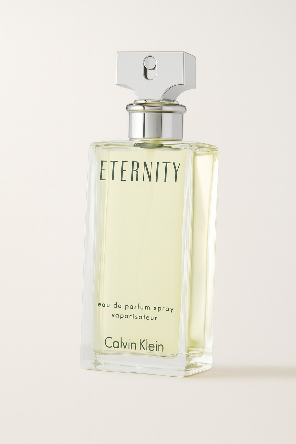 Eine schlichte, rechteckige Glasflasche von Calvin Klein Eternity Eau de Parfum Spray für Damen, mit zart gelber Flüssigkeit und silbernem T-förmigen Sprühkopf, stehend auf neutralem Hintergrund mit leichtem Schatten.