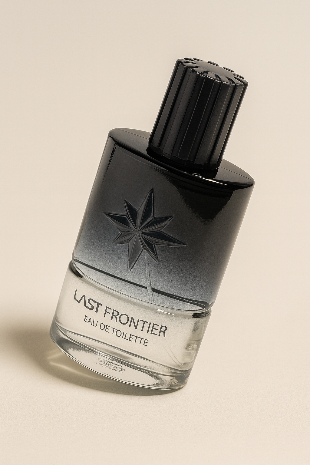 Ein modernes Parfumflakon mit dem Schriftzug „LAST FRONTIER Eau de Toilette“ steht leicht zur Seite gekippt auf einer neutralen beigen Fläche. Die zylindrische Glasflasche zeigt ein mattes Farbverlauf-Design von Schwarz zu Klar und ist mit einem eingeprägten Sternsymbol versehen. Der schwarze, geriffelte Deckel sitzt oben auf. Ein sanfter Schatten liegt seitlich darunter.