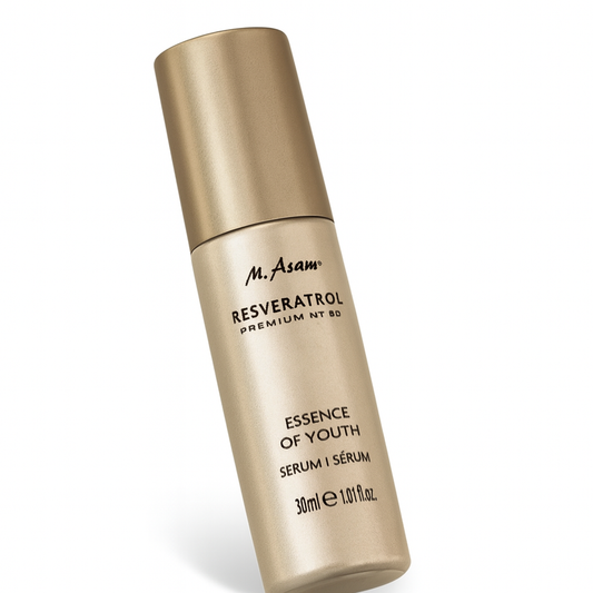 Eine goldfarbene, zylindrische Pumpflasche des M. Asam Resveratrol Premium NT50 Essence of Youth Serums liegt leicht schräg nach hinten gekippt auf weißem Hintergrund. Der Markenname und die Produktbeschreibung in schwarzer Schrift sind gut sichtbar, die Flasche wirft einen sanften Schatten.