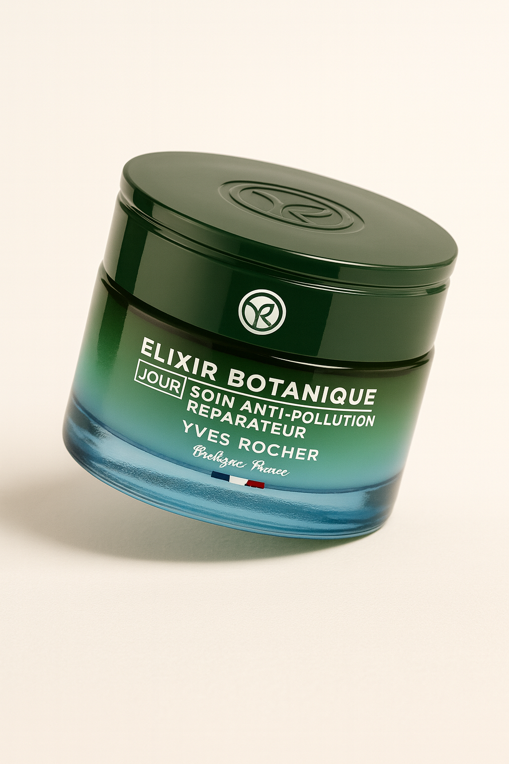 Ein runder grüner Tiegel der Yves Rocher Elixir Botanique Jour Anti-Pollution Repairing Care liegt leicht nach hinten geneigt auf neutralem Hintergrund. Das Glas zeigt einen Farbverlauf von Smaragdgrün zu Blau, die weiße Aufschrift ist klar lesbar, und ein sanfter Schatten verleiht Tiefe.